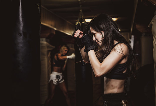 Dark photo of young pretty woman in dark gym, which has a training using punching bag.