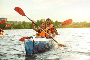 Happy young caucasian couple kayaking on river with sunset in the backgrounds. Having fun in...