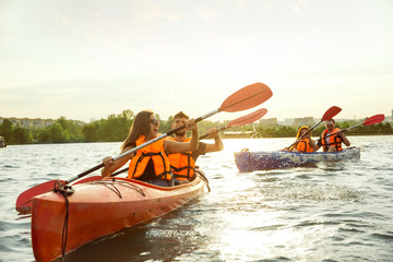Happy young caucasian group of friends kayaking on river with sunset in the backgrounds. Having fun in leisure activity. Happy male and female model laughting on the kayak. Sport, relations concept.