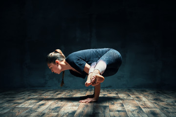 Young attractive woman practicing yoga doing side crane pose in dark room