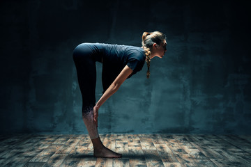 Young beautiful woman doing yoga asana half chair pose on dark room.