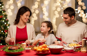 holidays, family and celebration concept - happy mother, father and little daughter having christmas dinner at home