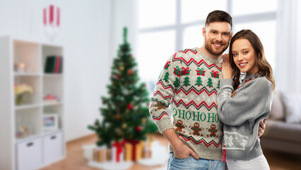 Fototapeta premium christmas, people and holidays concept - portrait of happy couple at ugly sweater party over home room background