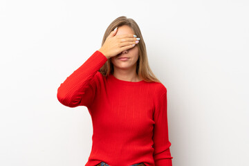 Young blonde woman with red sweater over isolated white background covering eyes by hands