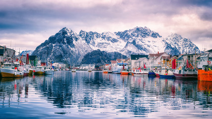 Fishing boats at harbour of cozy small fishing village Henningsvaer in Lofoten Islands, Northern Norway. Amazing landscape with mountains and reflection in the water, travel winter background - obrazy, fototapety, plakaty