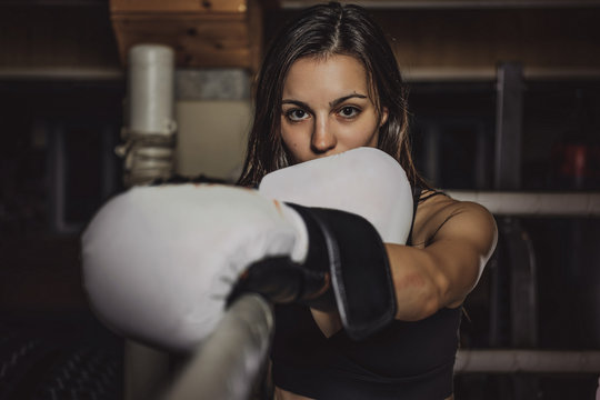 Young slim female boxer is ready to fight while standing at her corner on the ring.