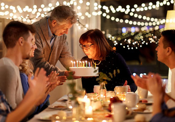 celebration and family concept - happy grandmother blowing candles on birthday cake at dinner party...