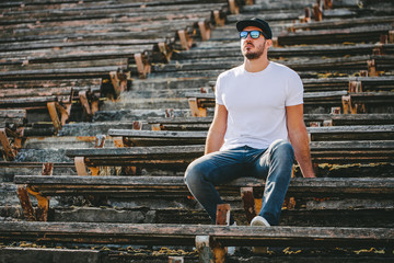 Hipster handsome male model with beard wearing white blank t-shirt and a baseball cap with space for your logo or design in casual urban style