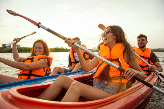 Happy young caucasian group of friends kayaking on river with sunset in the backgrounds. Having fun in leisure activity. Happy male and female model laughting on the kayak. Sport, relations concept.