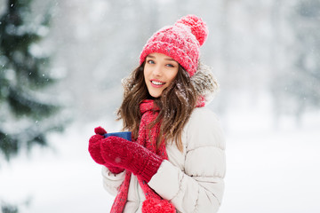 people, season and christmas concept - happy teenage girl or young woman with tea cup outdoors in winter park