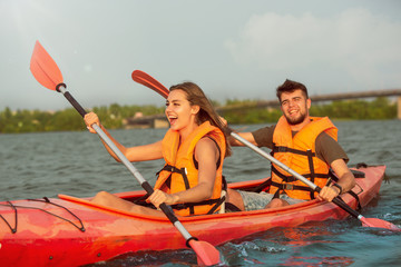Happy young caucasian couple kayaking on river with sunset in the backgrounds. Having fun in...