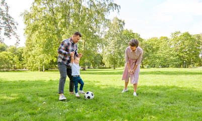 family, leisure and people concept - happy mother, father and little son with ball playing soccer at summer park