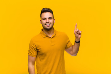 young hispanic man smiling cheerfully and happily, pointing upwards with one hand to copy space...