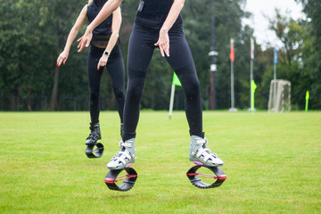 Fototapeta premium Girls in boots for jumping. Bouncing shoes on the legs of women. Sports performance on the football field in the rain. A new sport is jumping in special shoes on springs.
