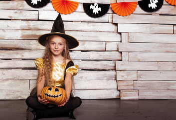 Little witch sitting with pumpkin by decorated wall