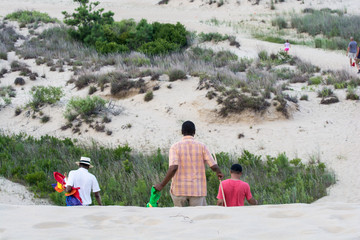 Family walking down sand dune at beach on family vacation at the Outer Banks in North Carolina.