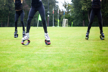 Obraz premium Girls in boots for jumping. Bouncing shoes on the legs of women. Sports performance on the football field in the rain. A new sport is jumping in special shoes on springs.
