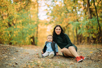 A mother and son sit on a pathway in autumn forest.