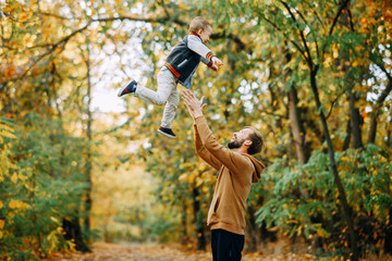 Father throws his son up while walking in the autumn forest.