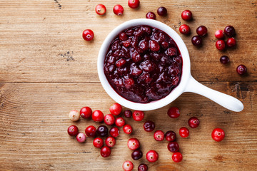 Cranberry sauce in ceramic saucepan with berries on wooden kitchen table from above.