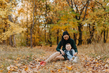 A mother and son sit on a pathway in the autumn forest.