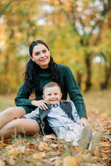 A mother and son sit on a pathway in the autumn forest.