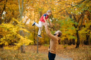 Father throws his son up while walking in the autumn forest.