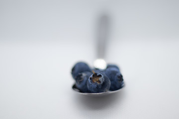 Some fresh and healthy blueberries on top of a spoon with white background