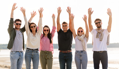 Obraz premium friendship, leisure and people concept - group of happy friends waving hands on beach in summer