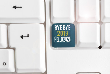 Conceptual hand writing showing Bye Bye 2019 Hello 2020. Concept meaning Starting new year Motivational message 2019 is over White pc keyboard with note paper above the white background © A