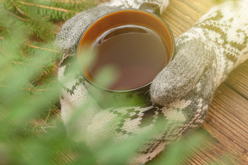 hands in mittens holding cup of tea close up on the brown brushed wooden background. Season winter autumn hygge, fika, lagom, cozy, warm, relax holidays concept
