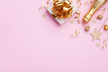 Flat lay background for Christmas or New year. Champagne bottle, gift or present box and golden confetti on pink top view.