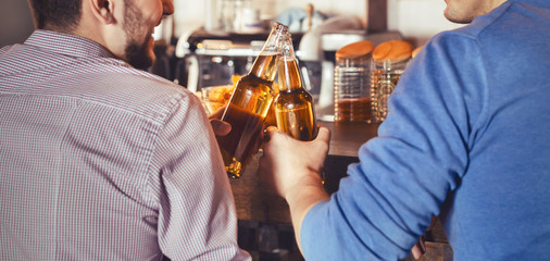 Mates Clinking Bottles Of Beer In Pub