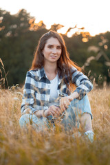 Beautiful young woman sitting on the grass at sunset and smiling