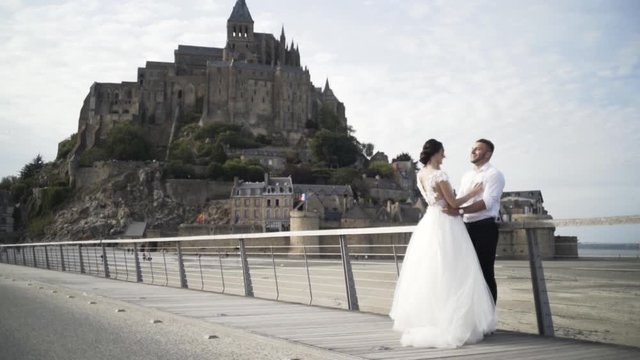 Beautiful photo of happy newlywed hugging couple. Action. Bride in a luxurious dress and the groom in white shirt and black trousers in front of the old beautiful castle in France