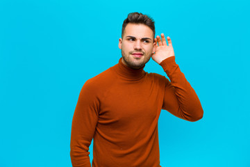 young hispanic man looking serious and curious, listening, trying to hear a secret conversation or...