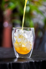 Pouring fresh orange juice on ice in glass on wooden table in a garden. Refresh your day.