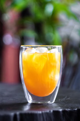 Fresh orange juice with ice in glass on wooden table in a garden. Refresh your day.