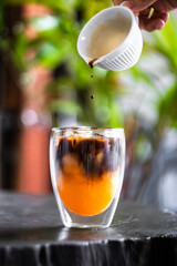 Iced fresh orange juice topped with espresso on wooden table in a garden; as sunrise coffee make a good day.