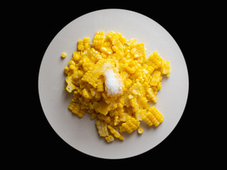 Boiled corn sprinkled with sugar in a white plate on a black background