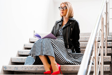 Young attractive blond woman makes some notes in violet notepad at library and sitting on ladder...