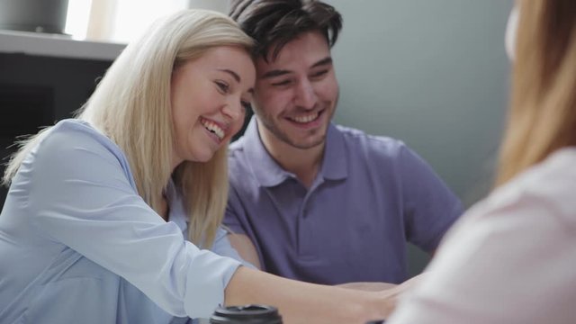 Delighted woman and man smiling and taking selfie then laughing while sitting near female colleague sipping coffee to go during break in office