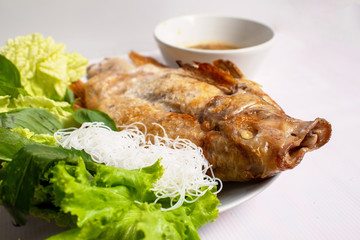 Grilled Tubtim fish placed on a plate of green vegetables with dipping sauce.