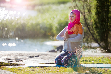 Attractive woman in hijab training in the park, meditating. Doing yoga exercises on fresh air and enjoying early morning. Healthy lifestyle