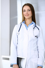 Doctor woman happy and cheerful while standing in hospital office at highlight background. Medicine and healthcare concept