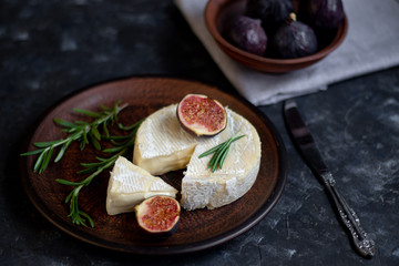 Ripe, beautiful, purple figs.  Sweet and juicy.  Mediterranean fruit is very healthy.  On a plate is Brie cheese.  There is empty space on a dark copyspace background.  Food for vegetarians.