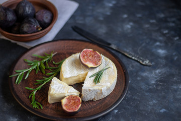 Ripe, beautiful, purple figs.  Sweet and juicy.  Mediterranean fruit is very healthy.  On a plate is Brie cheese.  There is empty space on a dark copyspace background.  Food for vegetarians.