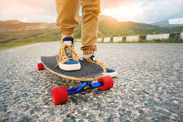 Close-up of male legs in rag sneakers on a longboard on the background of asphalt at sunset. Big skateboard with man legs. Youth leisure concept