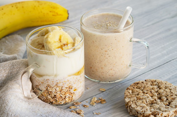 Two glass cups with ingredients banana, honey, oatmeal and yogurt and smoothie