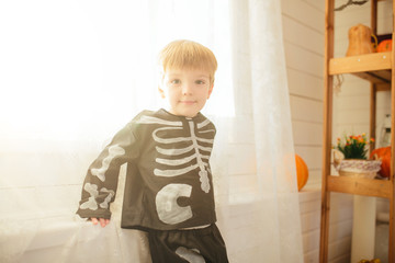 Little cute boy in a skeleton costume is ready for the celebration of Halloween in the room with the scenery for Halloween.